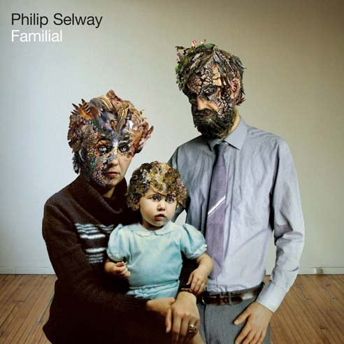 Surreal family portrait with figures wearing masks or headpieces made of organic materials.